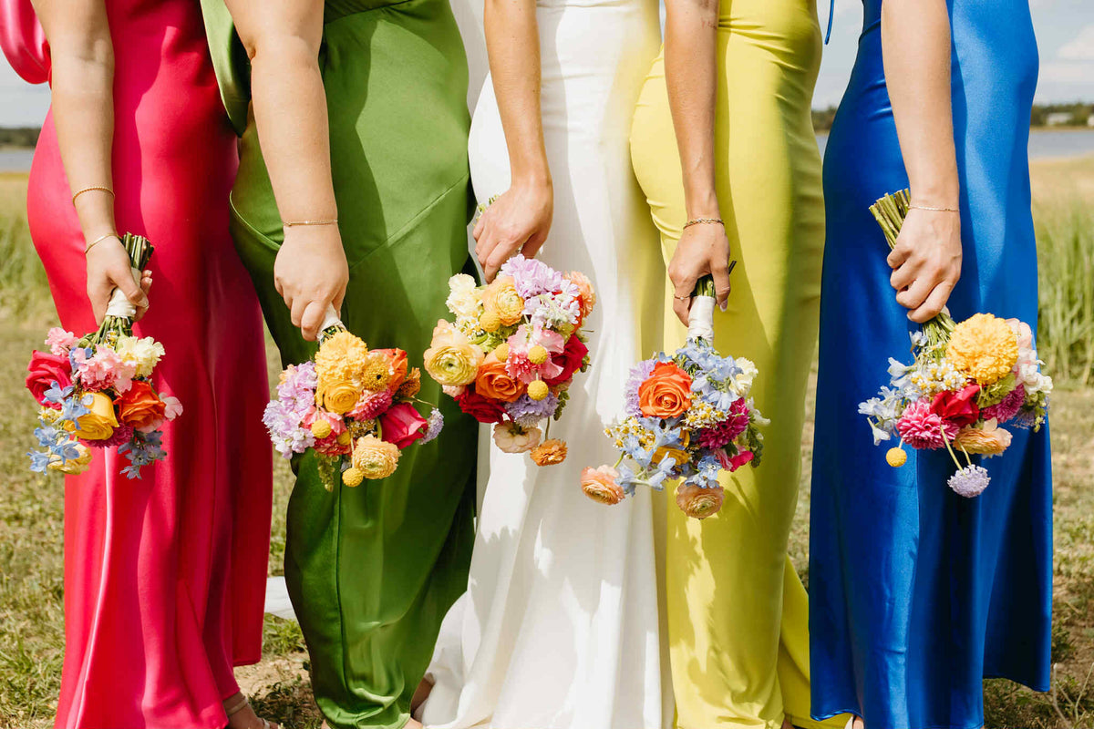 Five people in colorful outfits holding small floral bouquets in a field with romantique, light, colorful floral bouquet for european wedding made by Primavera floral Studio in Moncton, New brunswick.