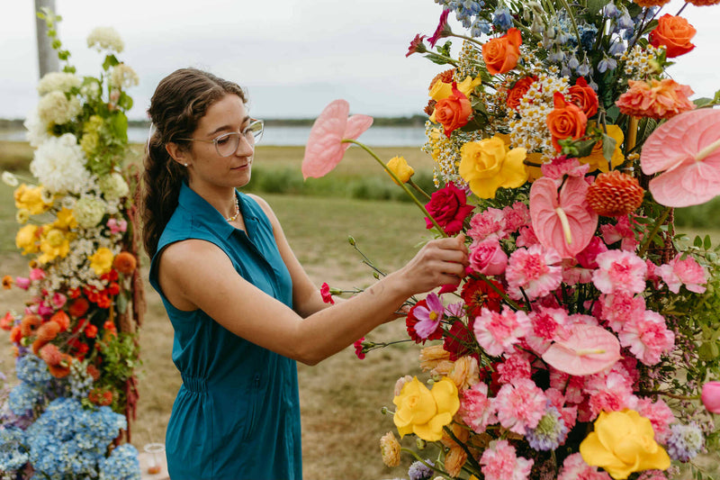 floral designer arranging flowers in a field with a large wedidng floral arrangement in the foreground, made in moncton New brunswick. Romantique, soft and colorful wedding flowers in Moncton