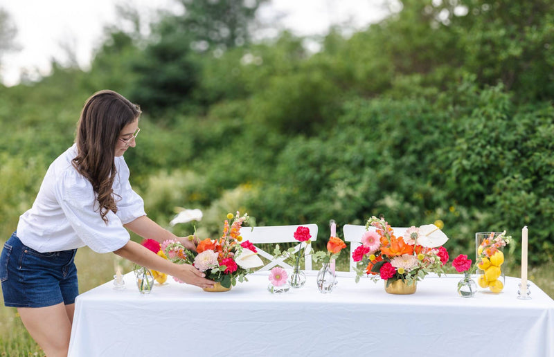 Julie, florist from Primavera floral studio, arranging event flowers on a table outdoors with greenery in the background. Flowers created in Moncton, New Brunswick.