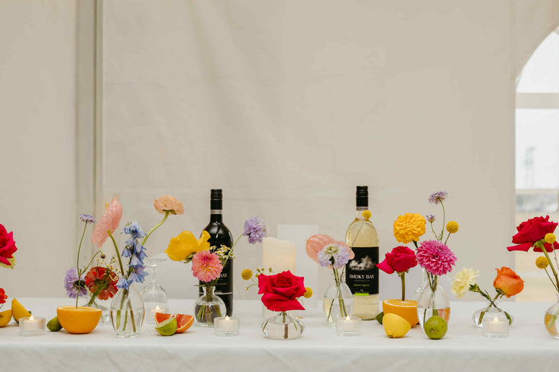 Flower setting with wine bottles and floral arrangements for a wedding on a white tablecloth made by wedding florist : Primavera floral studio in Moncton.