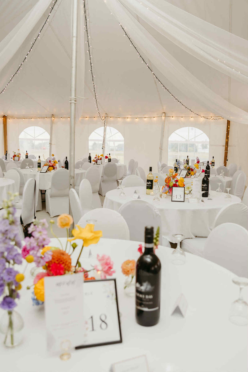 Decorated wedding flower reception with tables, chairs, and floral arrangements inside a white tent. Wedding flowers made by Primavera Floral studio, local flower shop to new brunswick. Colorful, modern, whimsical wedding florist.