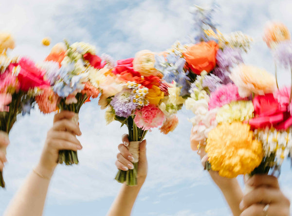 Three hands holding colorful flower bouquets against a clear blue sky Made by wedding florist in Moncton New brunswick.