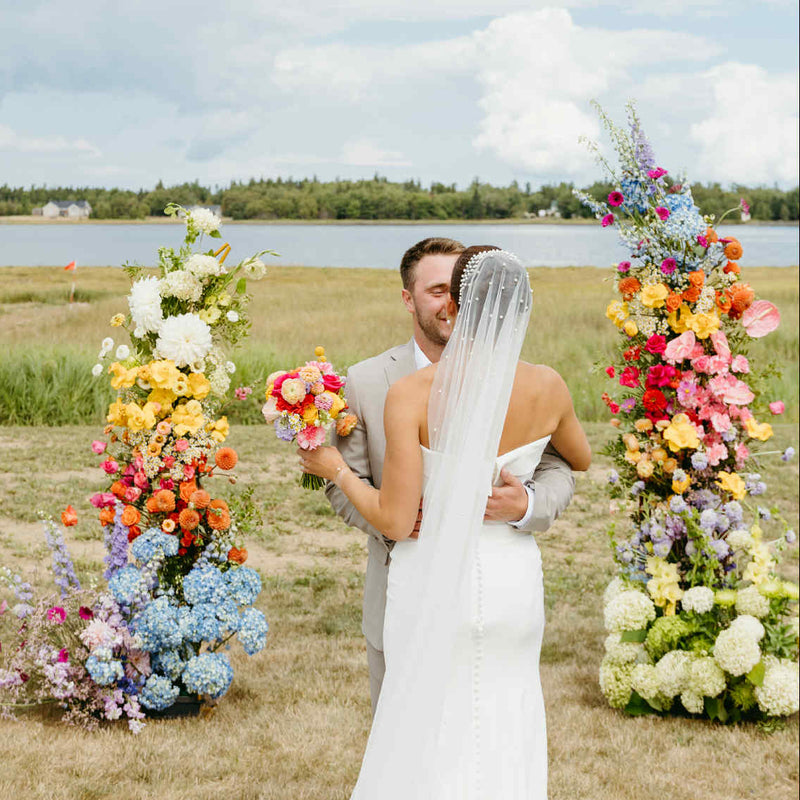 Couple holding hands in a field with colorful floral arrangements made by Primavera Floral studio, a wedding florist in Moncton, New brunswick for a modern wedding vendor in Moncton.