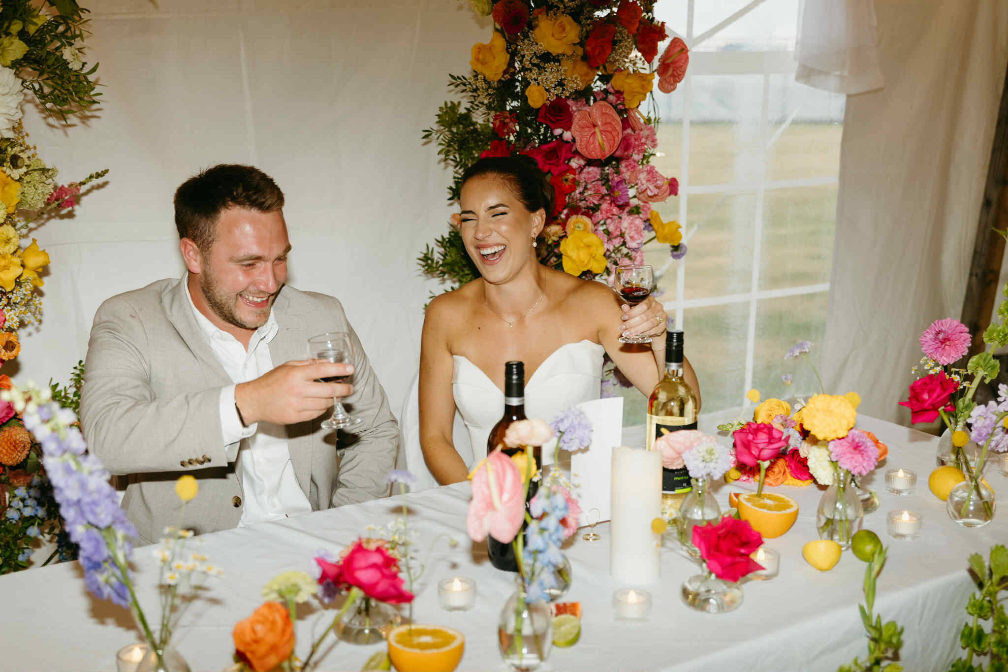 Couple sitting at a decorated wedding table with wedding flowers and wine glasses, smiling made by wedding florist Primavera Floral studio in Moncton New Brunswick.