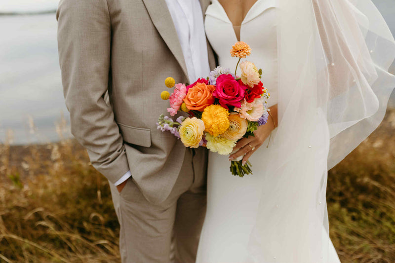 Couple in wedding attire standing in a field with a colorful floral bridal bouquet made by Julie Losier, local florist in Moncton , New Brunswick.